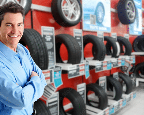 http://Tire%20dealer%20shop%20salesman%20standing%20in%20front%20of%20a%20rack%20of%20tires%20displayed%20in%20a%20showroom.