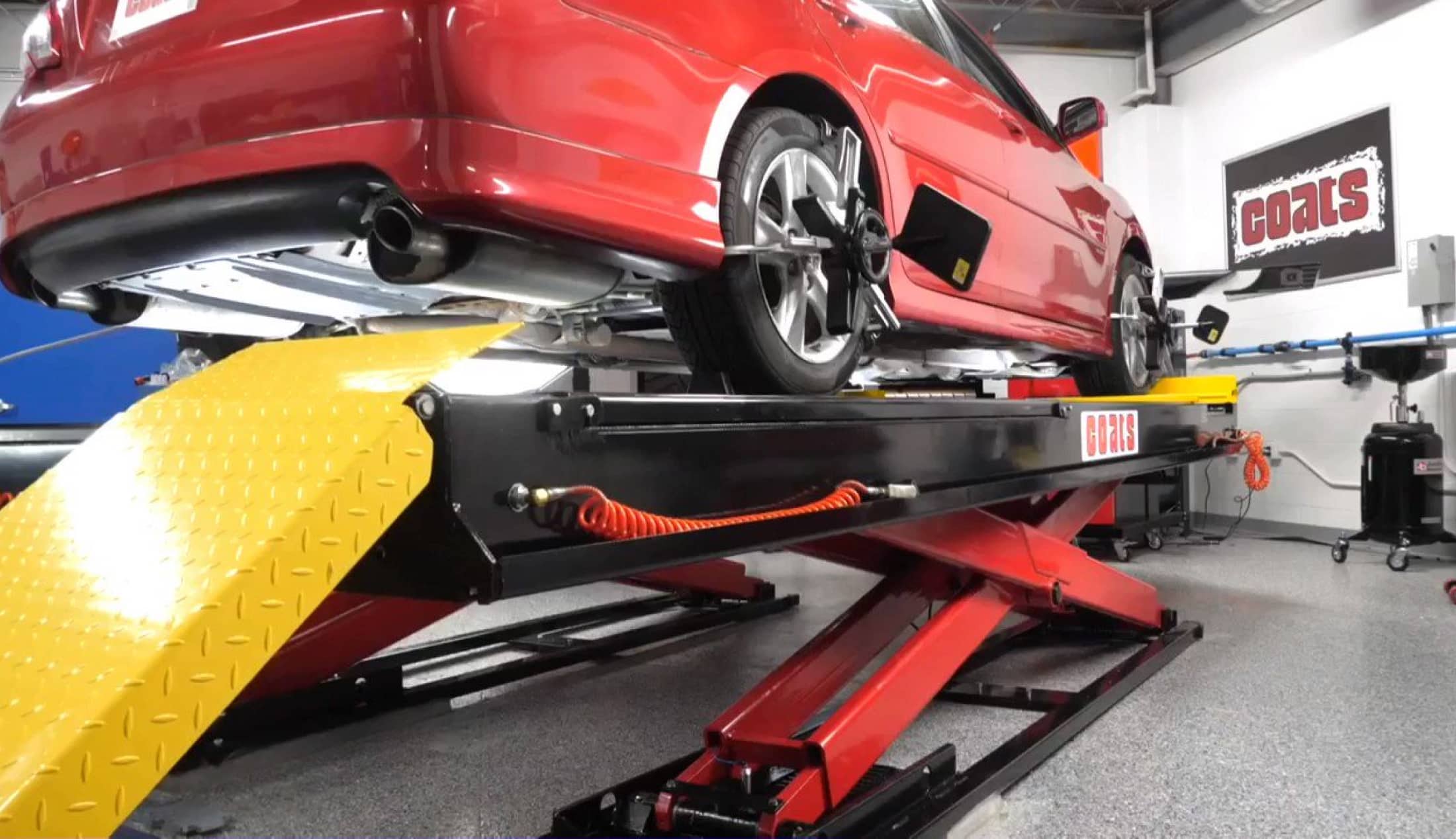 A red sedan is raised on a Coats alignment scissor lift in front of a Coats wheel aligne