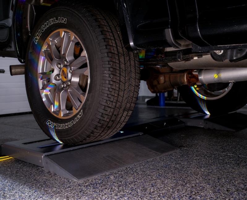 A Ford truck enters a garage and is about to drive over a Coats tread depth scanner mounted on the floor