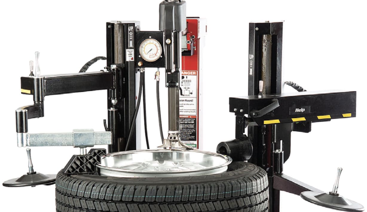 The top half of the 9028e tire changer, with arms ending in roller discs on the left and right sides of the tire changer, as well as a power roller that is resting on a tire on the tire changer tabletop
