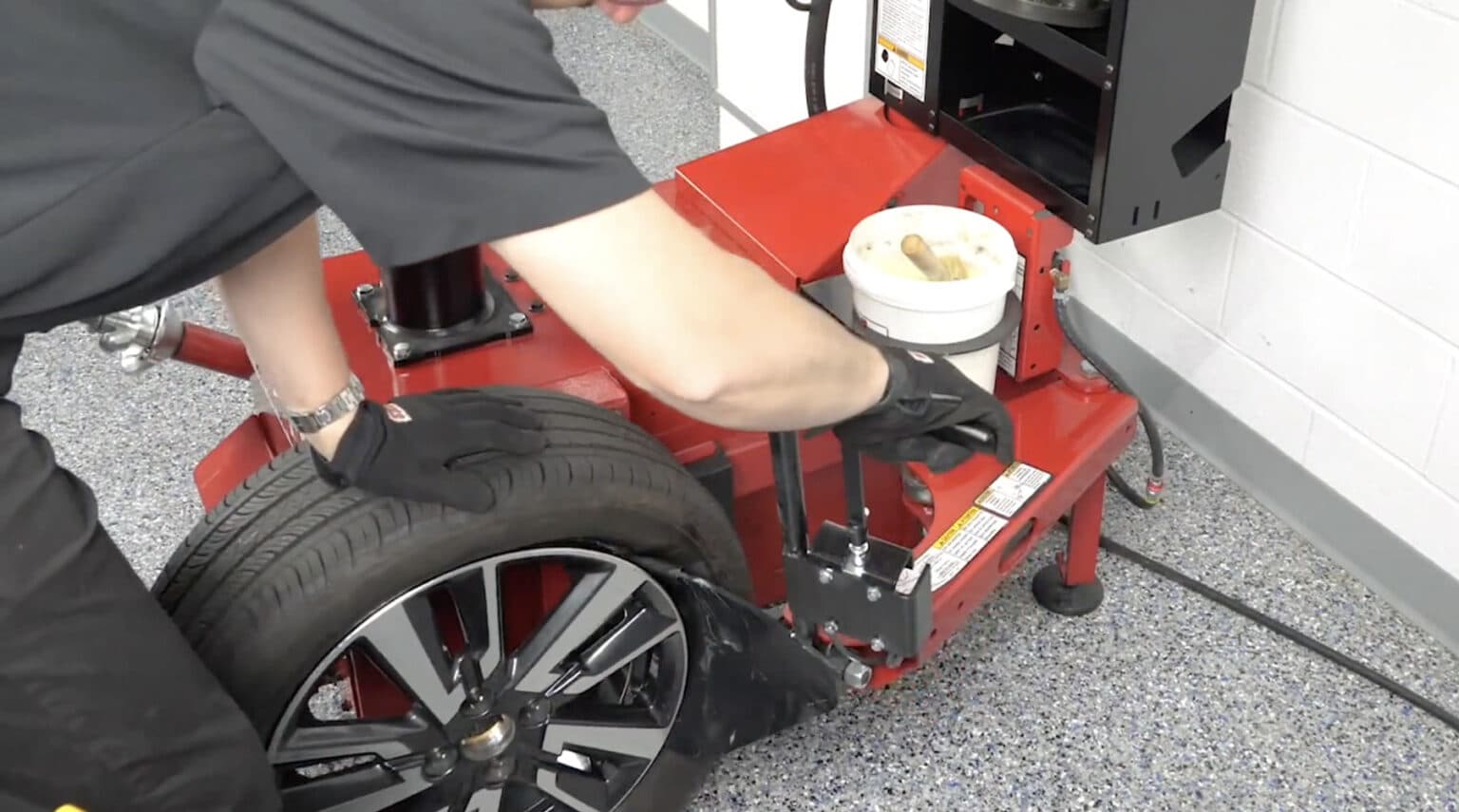 A technician uses his right hand to guide the bead loosener shovel between the wheel and the tire while his left hand holds the upright tire in place.