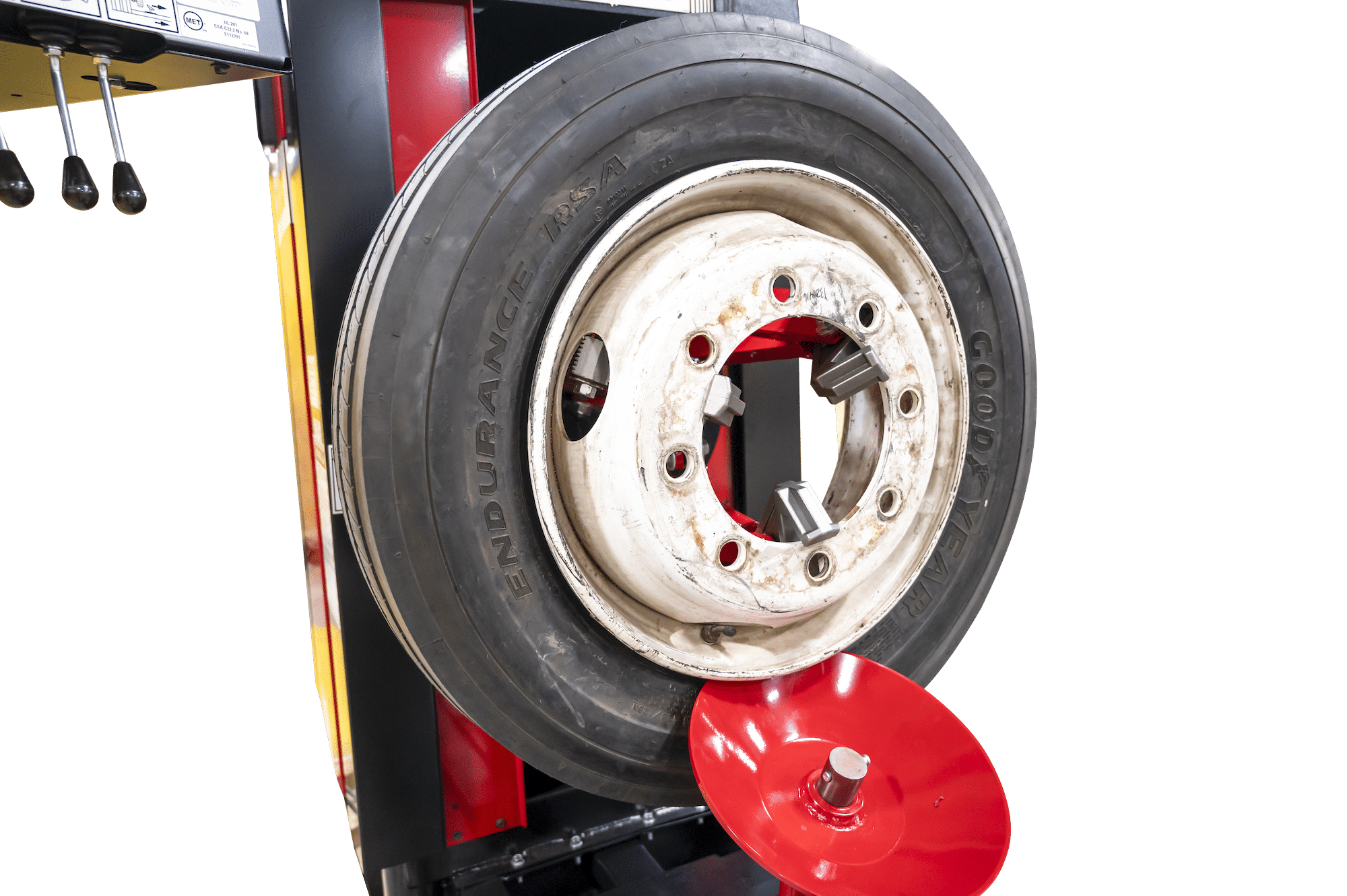A red disc shaped bead loosener loosens the bead of a tire mounted vertically on a heavy duty tire changer
