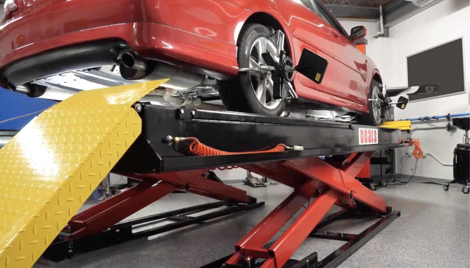 A red sedan is raised on a Coats alignment scissor lift in front of a Coats wheel aligner