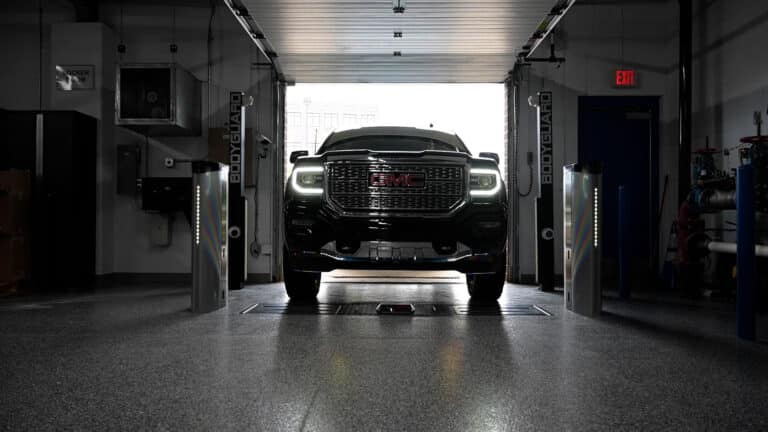 Alt text: A hero view of a black GMC truck slowly drives through a Coats inspection lane system with alignment check towers on each side of the truck.