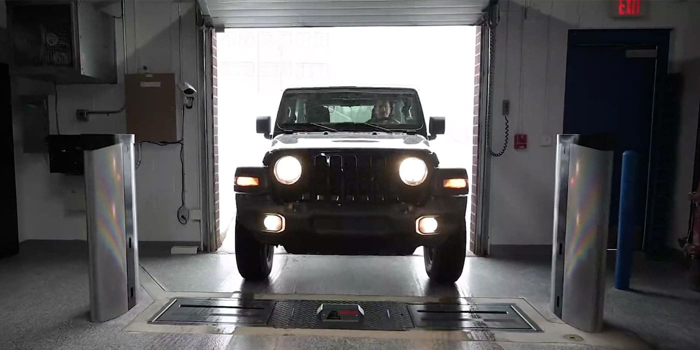 A Jeep Wrangler enters a service lane garage and drives between two alignment check towers and a flush mount Coats tread depth scanner in the ground