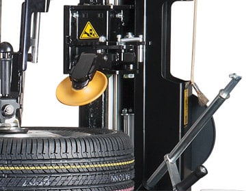 The moveable roller disc toward the back of the tilt back tire changer is angled downward at the tire on the tabletop