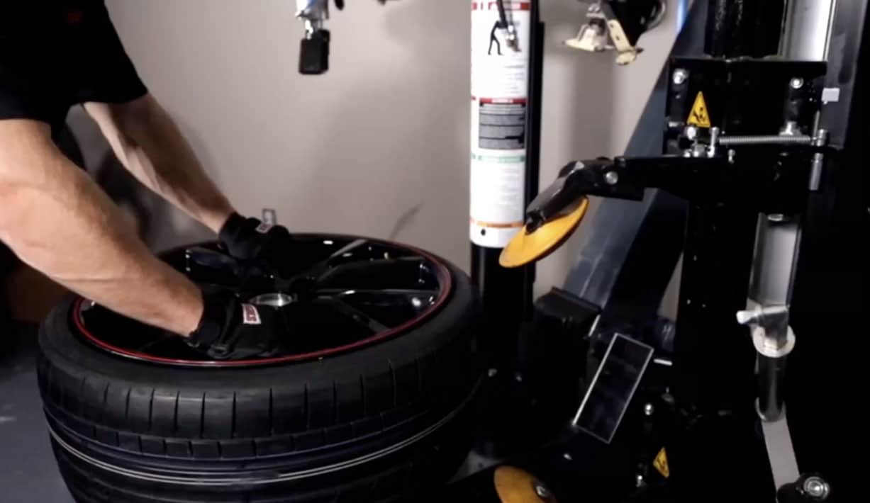 At technician has both hands on a tire, having just placed it on the tabletop of the APS 3000 tire changer