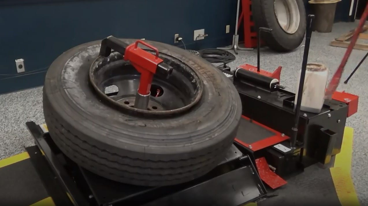 A technicians uses a tire bar to separate the tubeless tire from the wheel with the help of the combo tool on the HIT 6000 heavy duty tire changer, and a new tire is mounted onto the wheel