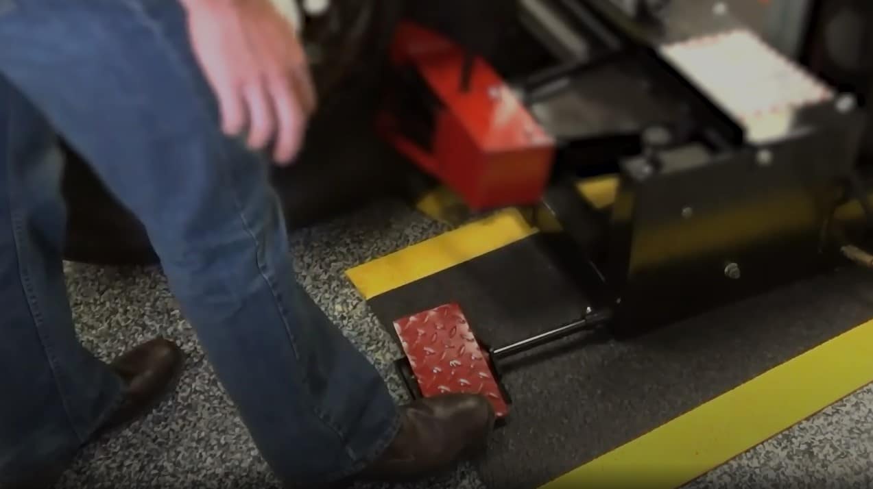 A technician uses his right boot to press on red floor pedals that can be pressed forward and backward to control the directions of the moving combo tool and the bead loosener