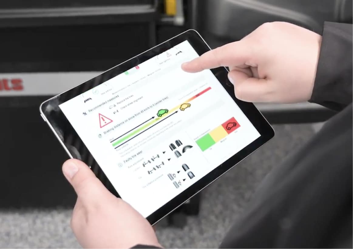 A technician holds a tablet horizontally to view the tire tread depth health report of a vehicle