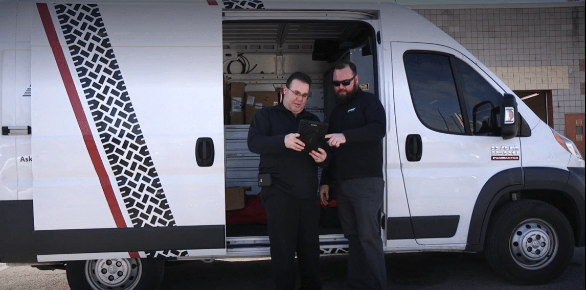 Two Coats Service Techs standing in front of a Coats service van looking at a tablet to find the next customer they will be servicing today.