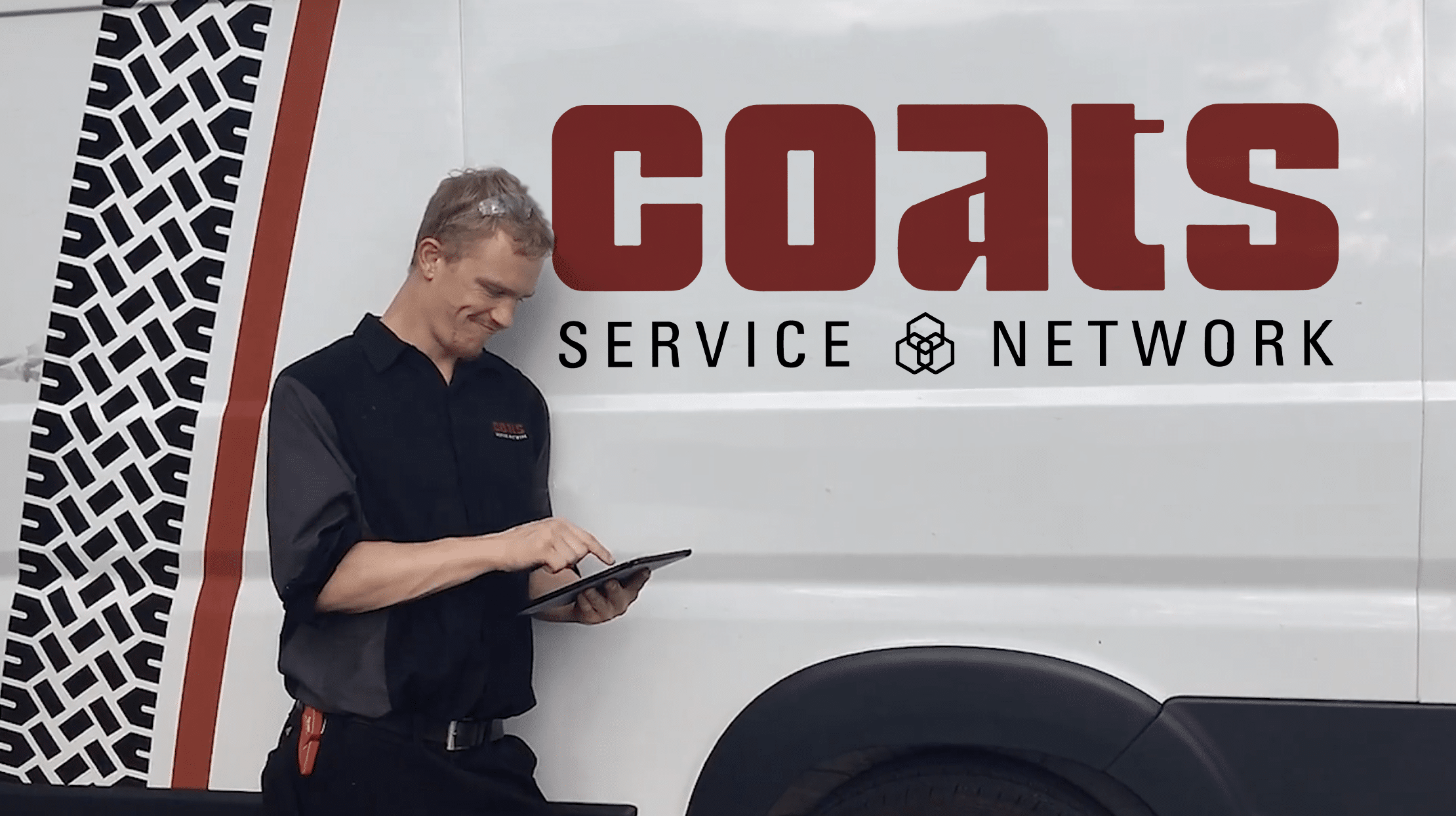 A Coats service technicians manages his customers service requests on an ipad while leaning against a service van that says Coats Service Network